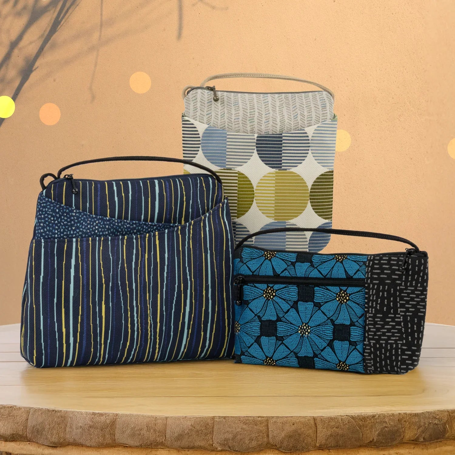 A group of small crossbody bags shown in the patterns Chevron Green, Eclipse Cool, and Filigree Gold.
